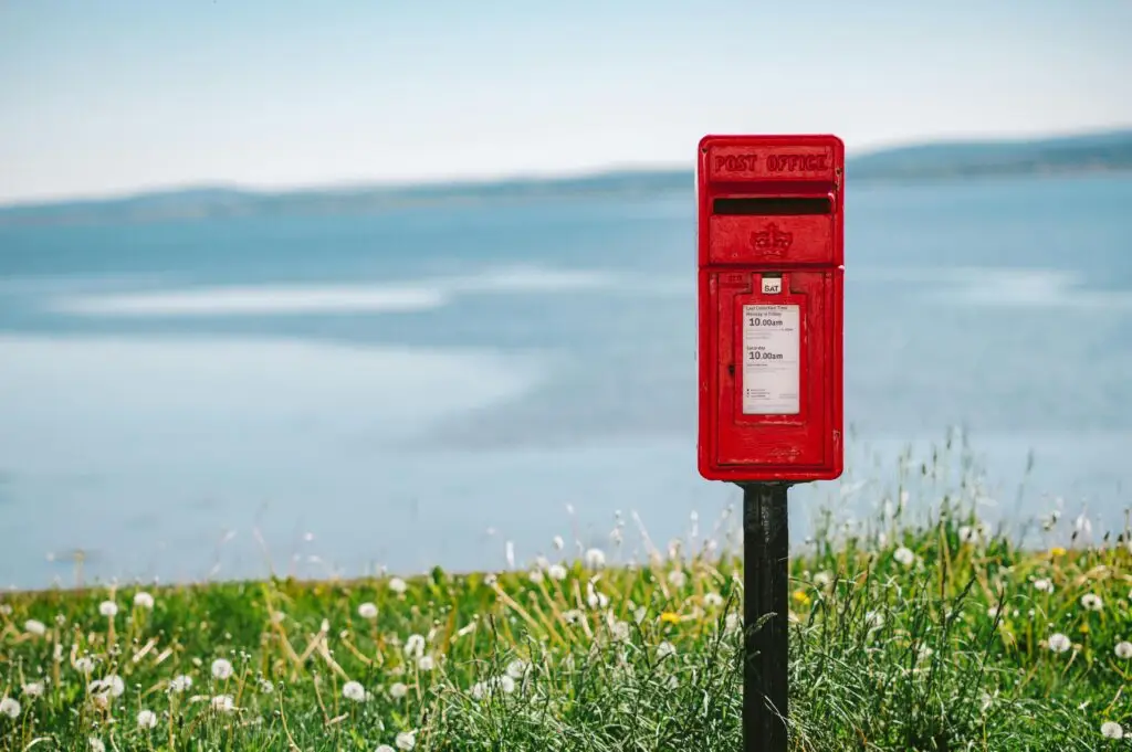 Red post box stands against the scenic coastal view in Avoch, Scotland.
